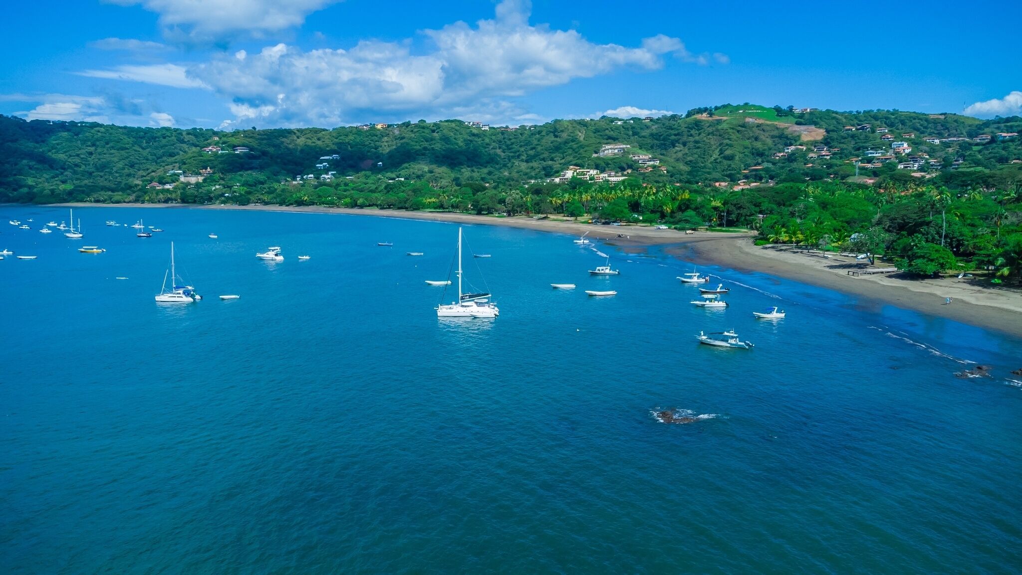 A coastal area with boats anchored near the shore, surrounded by lush greenery and hills in the background.