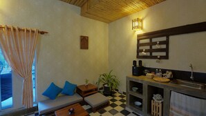 Ein gemütliches Zimmer mit kariertem Boden, einer Couch mit blauen Kissen, einem kleinen Tisch, einer Topfpflanze und einer Küchenzeile mit Spüle und Regalen.