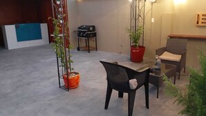 Un patio al aire libre con una mesa, sillas, una parrilla y plantas en macetas.