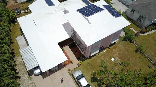 A modern building with solar panels on the roof, a covered parking area, and a small garden.