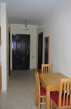 A dining area with a table and four chairs, each with a cushion, features a door and a ceiling fan.