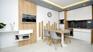 Une cuisine moderne avec des armoires blanches, un mur d’accent en bois et un coin repas comprenant une table en bois et des chaises grises.