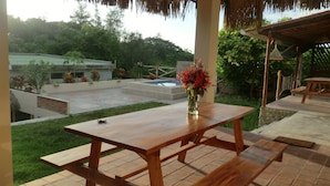 Una mesa de madera con un florero, una hamaca y una piscina al fondo.