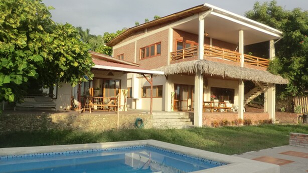Una casa de dos pisos con piscina, un patio cubierto y una escalera que lleva al piso superior.