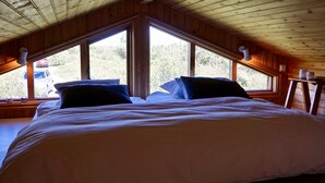 A bedroom with a large bed, two windows, and a wooden ceiling.