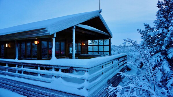 A log cabin with a snow-covered deck and large windows.