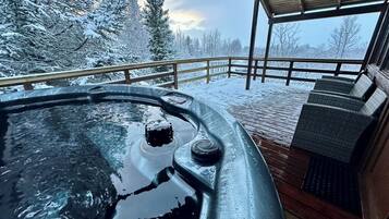 Uma banheira de hidromassagem com deck de madeira, rodeada por árvores cobertas de neve.