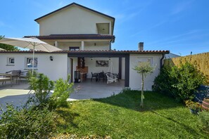 Una casa de dos pisos con un patio, mobiliario exterior y un pequeño jardín.
