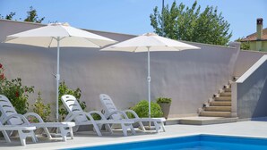 Una piscina con sillones blancos y sombrillas, una escalera de hormigón y una pared color beige.