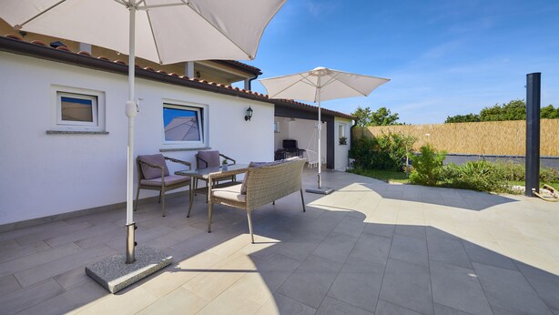 Un patio al aire libre con dos sombrillas blancas, una silla de mimbre y una mesa.