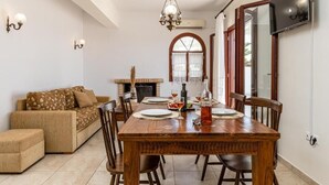 A dining area with a wooden table set for four, surrounded by chairs. There is a sofa with a patterned cover in the background.