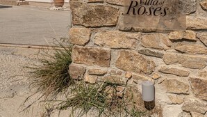 A stone wall with a sign reading 'Villa of Roses' in front of a white building with arched windows and a red roof.