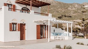 A two-story white building with wooden shutters, a covered outdoor seating area, and a mountainous backdrop.