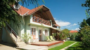 A two-story house with a red-tiled roof, a balcony with wooden railings, and a front porch with two chairs. - Casa Lavanda Alsóörs - Holiday home with pool (Alsóörs)