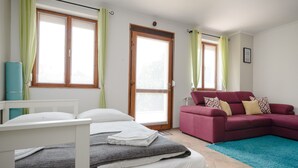 A bedroom with a bed, a red sofa, and two windows with curtains. - Casa Lavanda Alsóörs - Holiday home with pool (Alsóörs)
