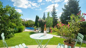 A patio with a round table, two chairs, a bottle, and two wine glasses. - Casa Lavanda Alsóörs - Holiday home with pool (Alsóörs)