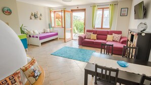 A cozy living room with a red sofa, a white chair, a dining table, and a blue rug. - Casa Lavanda Alsóörs - Holiday home with pool (Alsóörs)