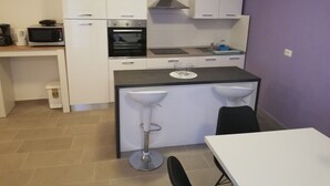 A compact kitchen with white cabinets, a black oven, a microwave, and a sink. There is a small bar stool and a white table.