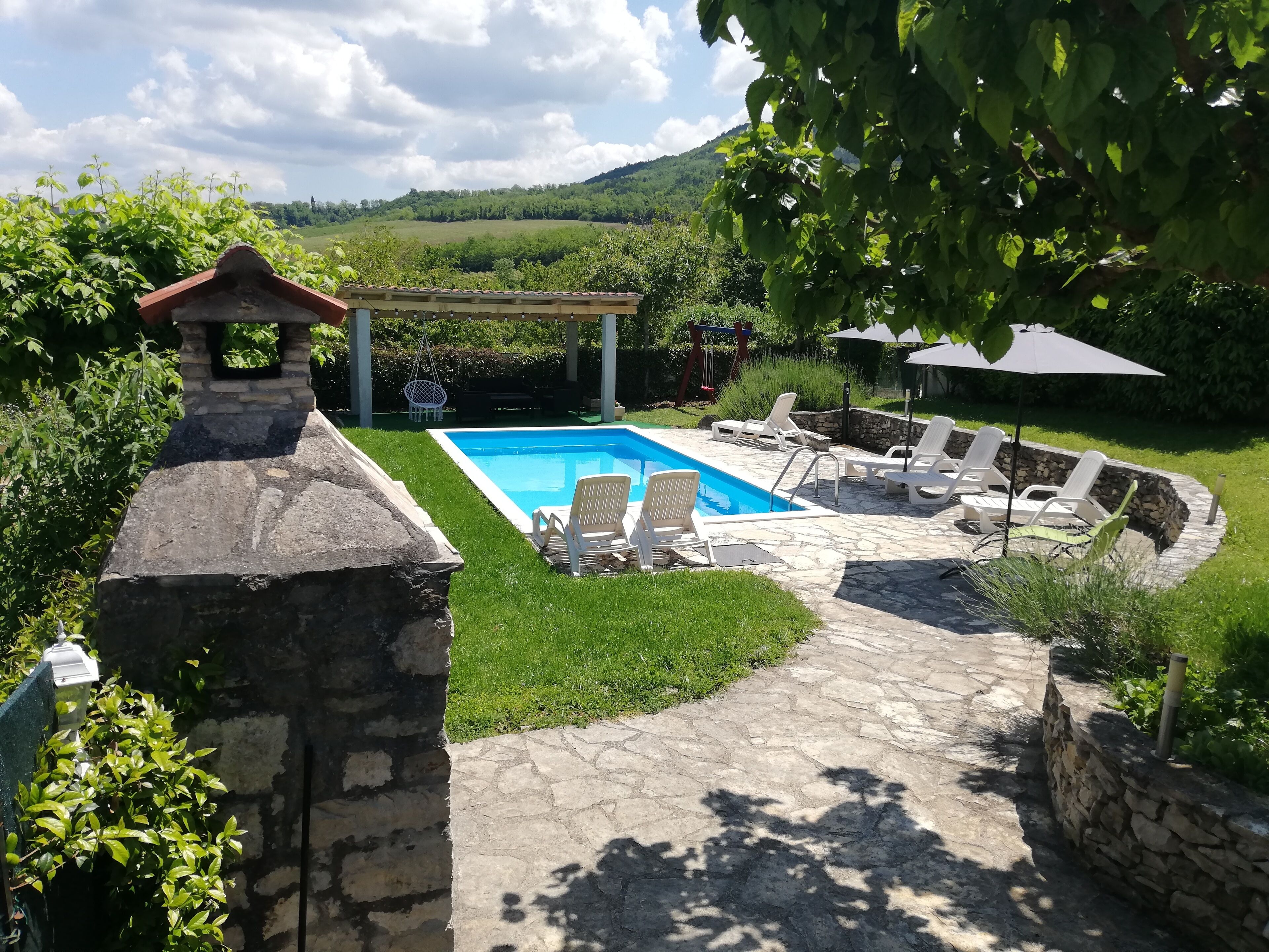 A backyard with a swimming pool, stone patio, and lounge chairs.