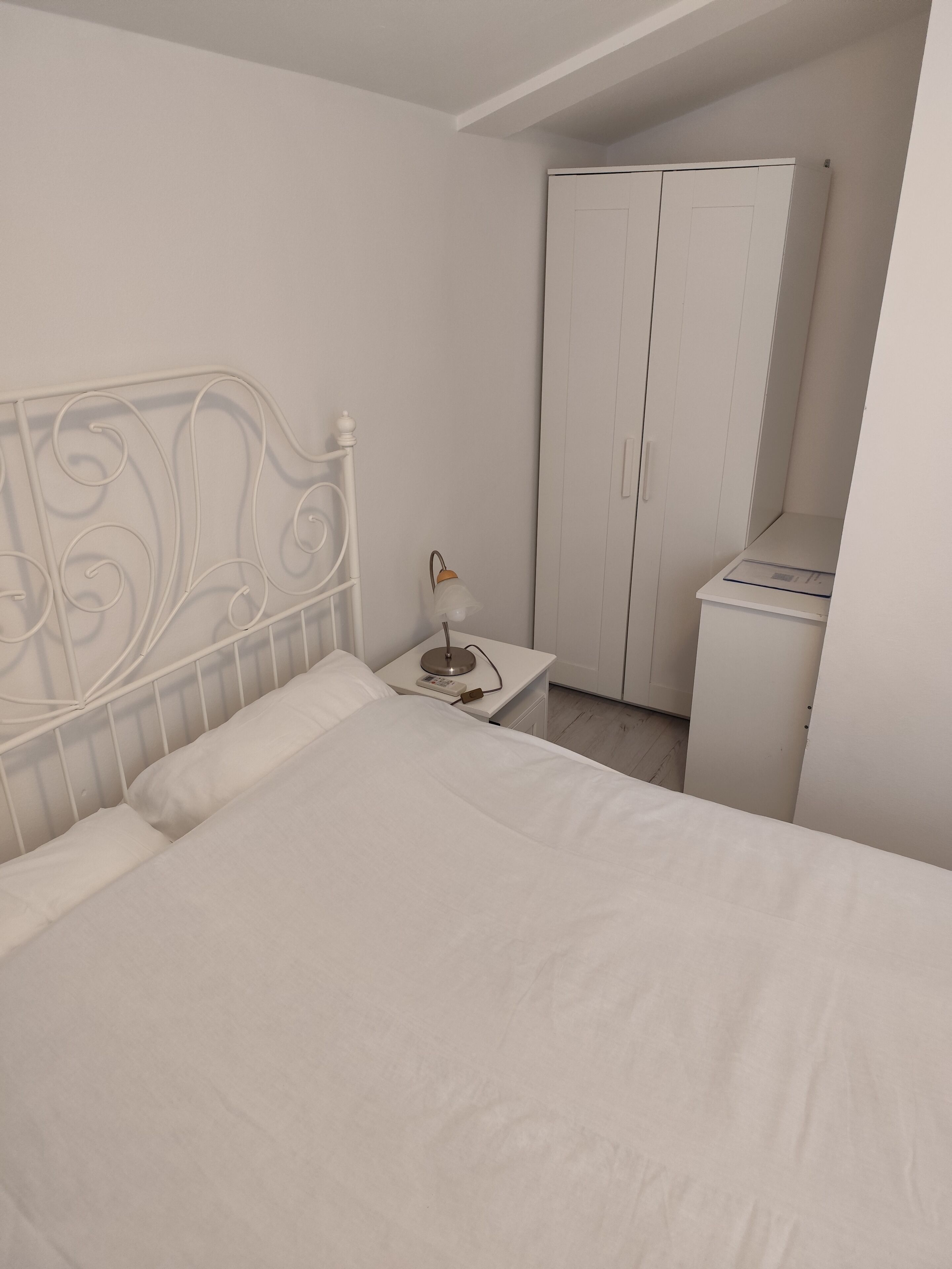 A bedroom with a bed, a nightstand, a lamp, and a wardrobe.