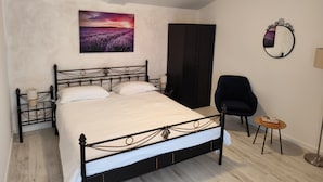 A bedroom with a bed, a chair, a small table, a wardrobe, and a painting on the wall.