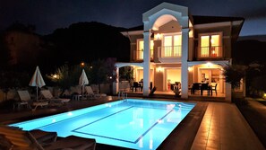 A two-story house with a swimming pool, outdoor seating, and a well-lit patio area.
