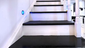 A staircase with white walls and black steps, leading to a landing with a white railing.