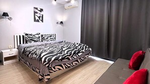 A modern bedroom with a zebra-patterned bed, a brown sofa with red cushions, a unique chandelier, and a wall-mounted air conditioner.