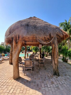 A thatched gazebo with a pool and lounge chairs in the background. - Apartment in Playa Chaca Complex near downtown Progreso  (Progreso)