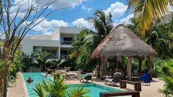 A pool area with lounge chairs, a thatched umbrella, and palm trees.
