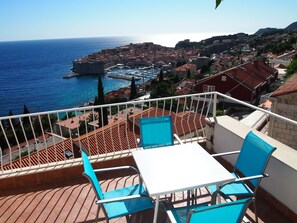 A terrace with a table and chairs overlooking a coastal town with historic buildings and a harbor. - Attic Apartment With Breathtaking Old City View (Dubrovnik)
