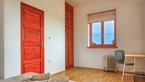 Ein Schlafzimmer mit Holzboden, einem Bett mit gerollten Handtüchern, einem Schreibtisch mit Stuhl, einem Fenster mit Blick und einem Heizkörper.