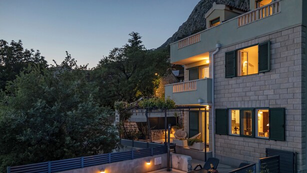 A modern two-story building with a rooftop pool, outdoor seating, and a balcony.