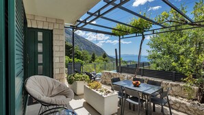 A terrace with a table and chairs, a potted plant, and a view of the sea.