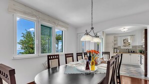 A dining area with a round table, chairs, a chandelier, and a view of the outdoors.