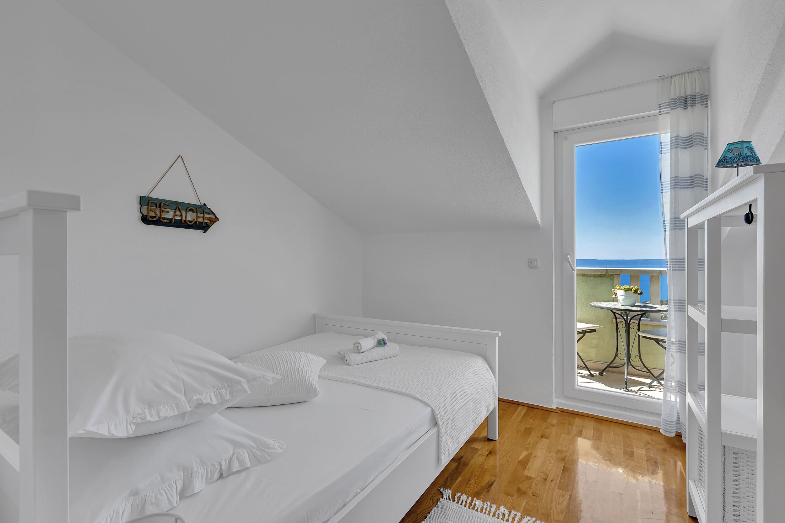 Quarto com cama, janela com vista para o exterior e uma pequena varanda com mesa e cadeiras.