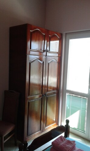 Une pièce comprenant une grande armoire en bois, une chaise et une fenêtre avec des stores.