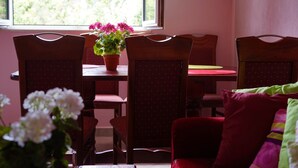 A dining area with wooden chairs and a table, a potted plant with flowers, and a window with a view of greenery. - Apartment Bella Vista With Sea View Montenegro  (Radovići)
