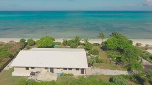 A beachfront property with a white building, clear turquoise waters, and lush greenery. - Corktree Beach House - Modern, Beachfront 2bd/3ba home with central AC (Grand Turk)