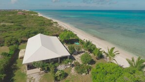 An aerial view of a coastal property with a white-roofed building, a sandy beach, and clear turquoise waters. - Corktree Beach House - Modern, Beachfront 2bd/3ba home with central AC (Grand Turk)