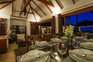 Comedor con mesas dispuestas para una comida, con vista al exterior al atardecer.