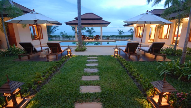 A resort pool area with lounge chairs and umbrellas, a clear view of the ocean, and a well-maintained garden path.