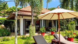 A resort with a covered outdoor seating area, palm trees, and potted plants.