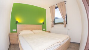 Un dormitorio con cama, mesitas de noche, una pared verde, una ventana con cortinas y un radiador.