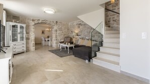 A spacious living area with a stone wall, a staircase, and a dining area. - VILLA NARESTE Stone house with pool and amazing sea view (Jesenice)
