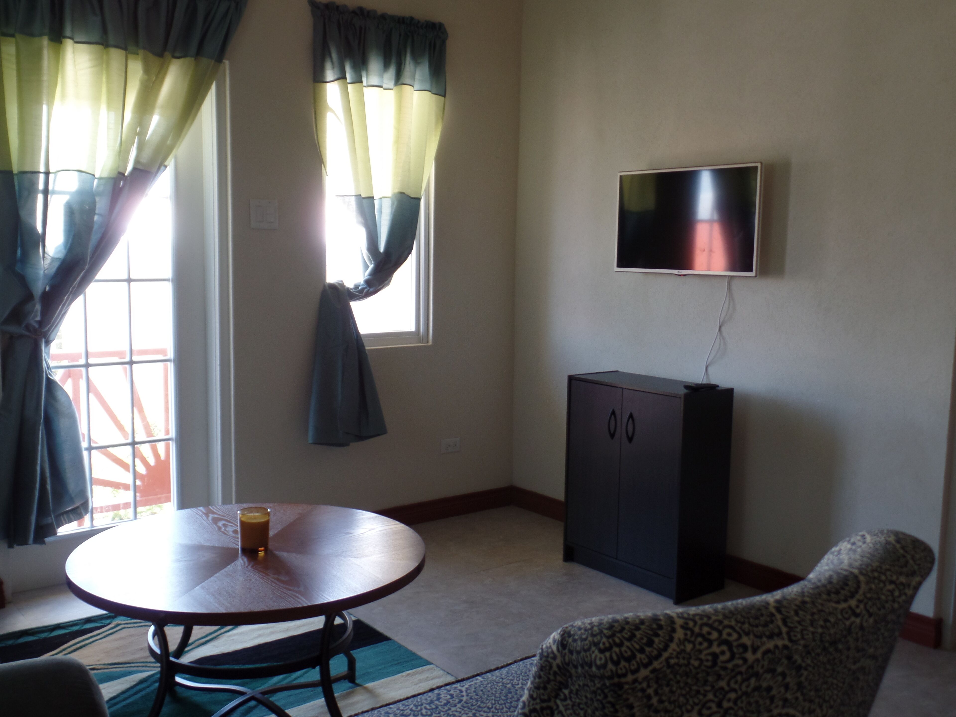 A room with a round table, a cabinet, a patterned armchair, and a TV mounted on the wall.