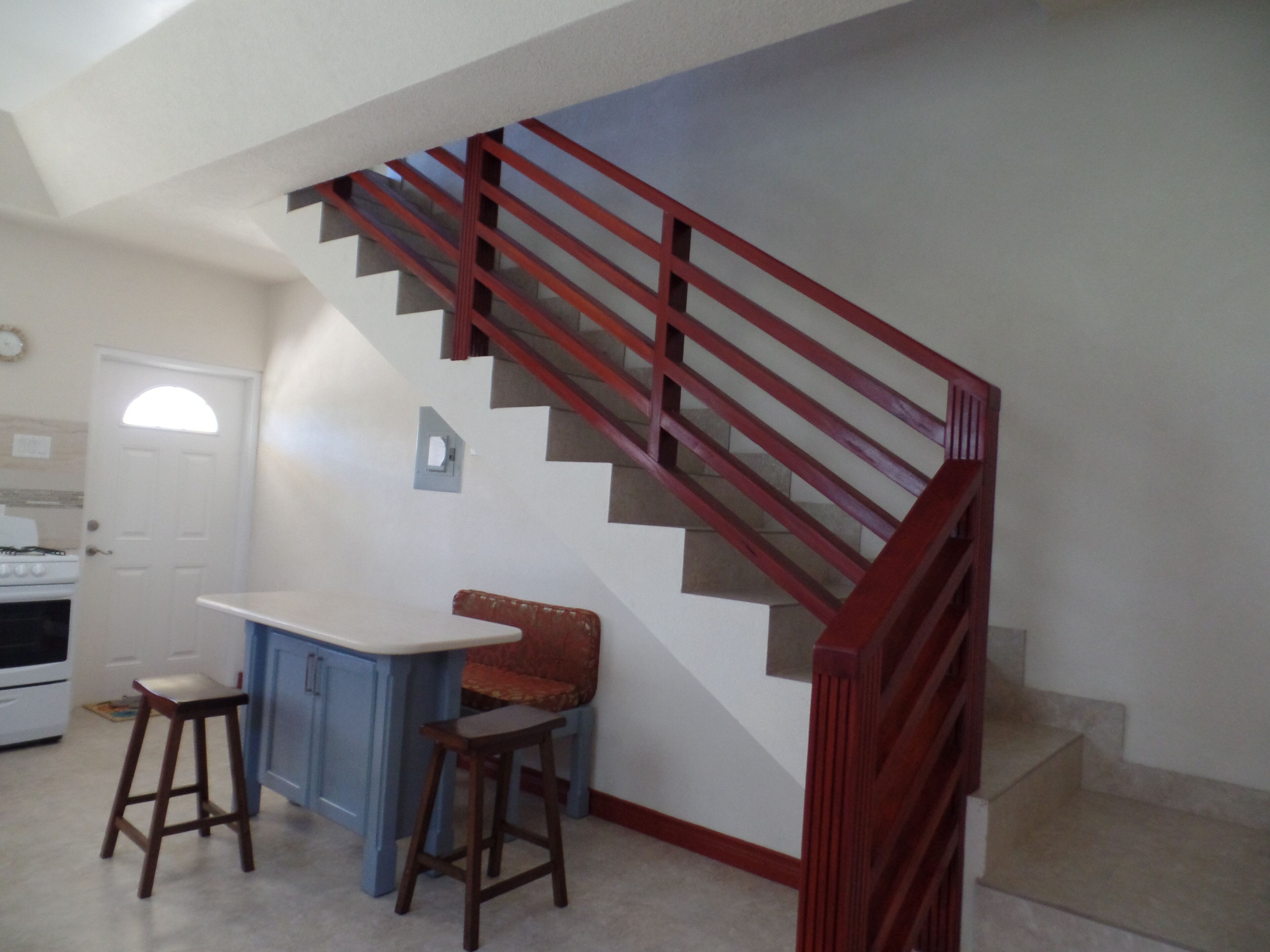 A kitchen with a white countertop, two stools, a stove, and a red staircase.