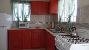 A compact kitchen with red cabinets, a white stove, a microwave, and a sink. - Great location for the adventurous traveler! (Maxwell)