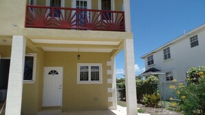A two-story building with a yellow facade, a red balcony railing, and a white door. - Great location for the adventurous traveler! (Maxwell)