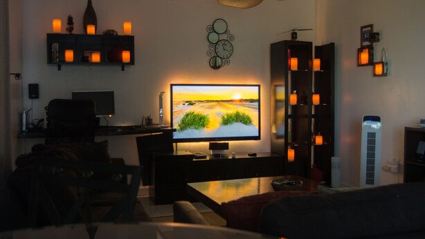 Una sala de estar con televisor de pantalla plana, ventilador de techo y estantería con velas.